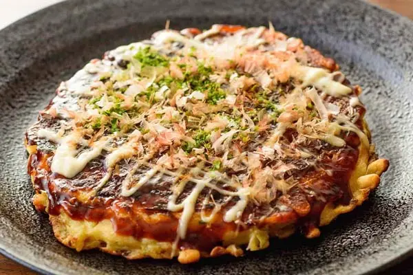 Okonomiyaki cocinado a la parrilla con ingredientes frescos.